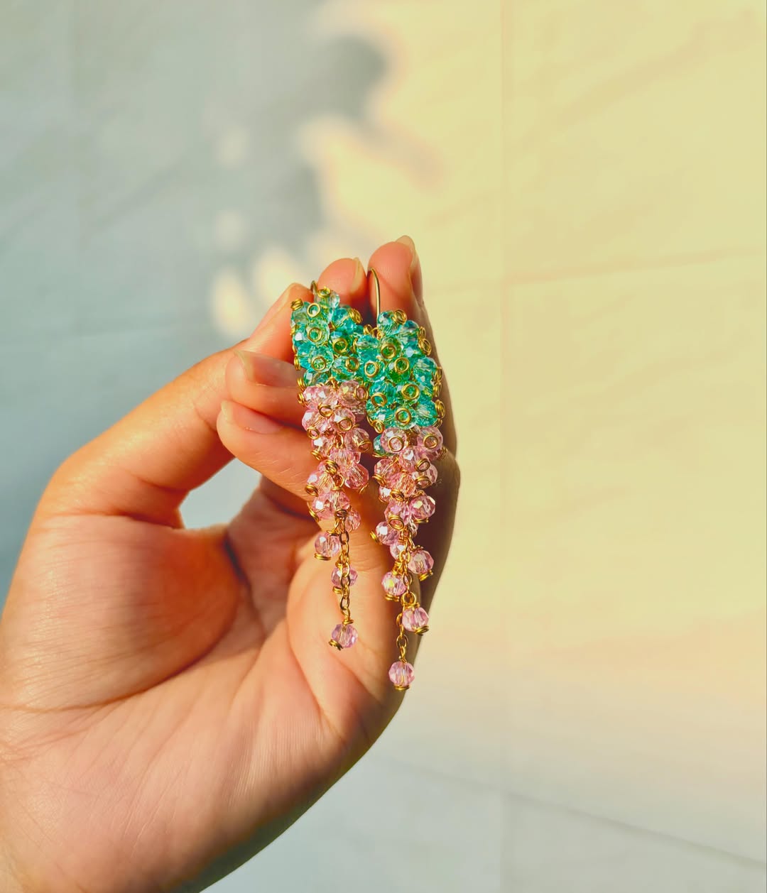 The Flora Drops — teal and rose crystal cascade earrings held in hand