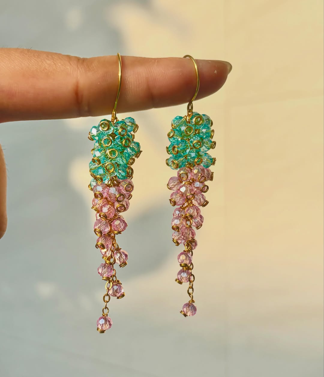 Handcrafted crystal cascade earrings in teal and rose, catching golden hour light
